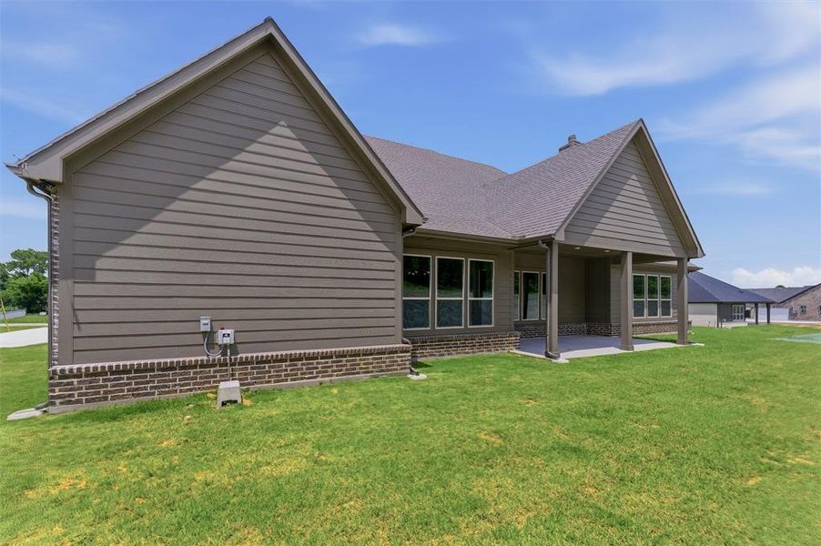 Expansive green lawn with a covered patio, featuring a brick foundation and siding exterior