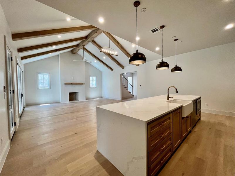 Kitchen with light hardwood / wood-style flooring, light stone counters, an island with sink, sink, and beam ceiling