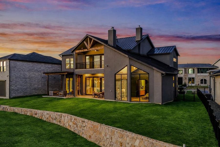 Back of property at dusk with a standing seam roof, a chimney, a patio area, and a balcony
