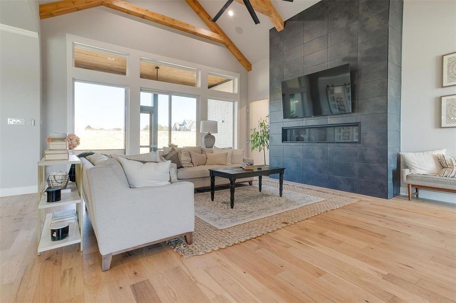 Living room with a tile fireplace, high vaulted ceiling, ceiling fan, light wood-type flooring, and beamed ceiling