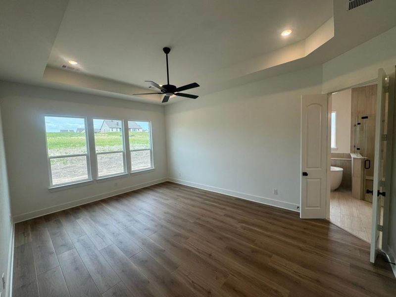 Spacious room featuring wood-finish flooring, a tray ceiling with recessed lighting, and a ceiling fan