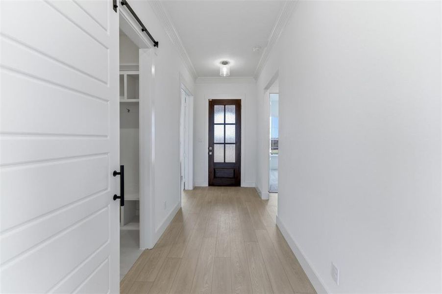 Entryway with a barn door, ornamental molding, and wood finished floors