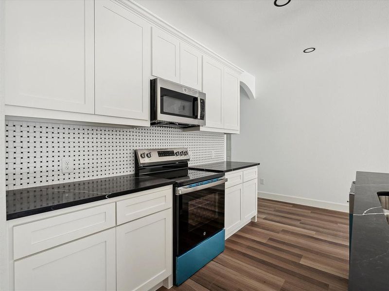 Kitchen with appliances with stainless steel finishes, white cabinetry, tasteful backsplash, and dark hardwood / wood-style floors