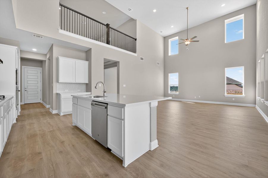Kitchen with a towering ceiling, white cabinetry, an island with sink, ceiling fan, and light wood finished floors
