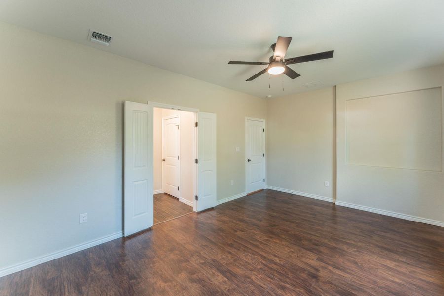 Spacious room featuring wood-finish flooring, light-toned walls, a ceiling fan with integrated lighting, and white trim