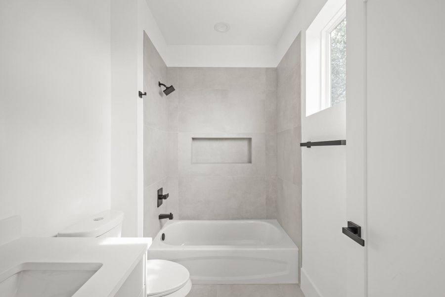 A transom window shines light onto the combination tub/shower which has tile surrounded walls as well as a built-in niche for soap and shampoo. A transom window shines light onto the combination tub/shower which has tile surrounded walls as well as a built-in niche for soap and shampoo.