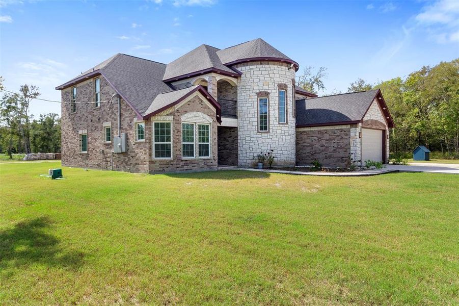 This spacious brick and stone home features a unique turret design, large windows, and a neatly landscaped lawn. It offers a two-car garage and sits in a serene, wooded area, providing both privacy and natural beauty.