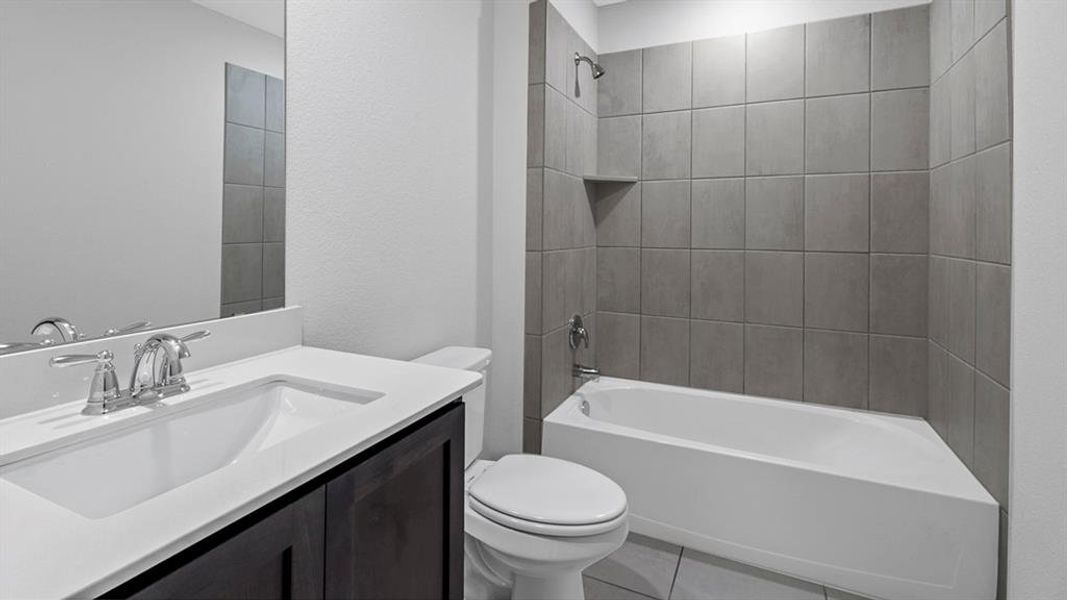 Bathroom featuring a bathtub with gray tiled surround, a built-in shower niche, and a vanity with a white countertop and dark cabinetry Bathroom featuring a bathtub with gray tiled surround, a built-in shower niche, and a vanity with a white countertop and dark cabinetry