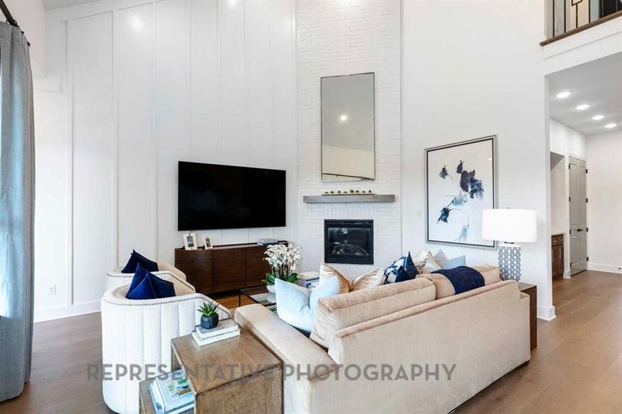 Living area featuring wood finished floors, a brick fireplace, a high ceiling, and recessed lighting Living area featuring wood finished floors, a brick fireplace, a high ceiling, and recessed lighting
