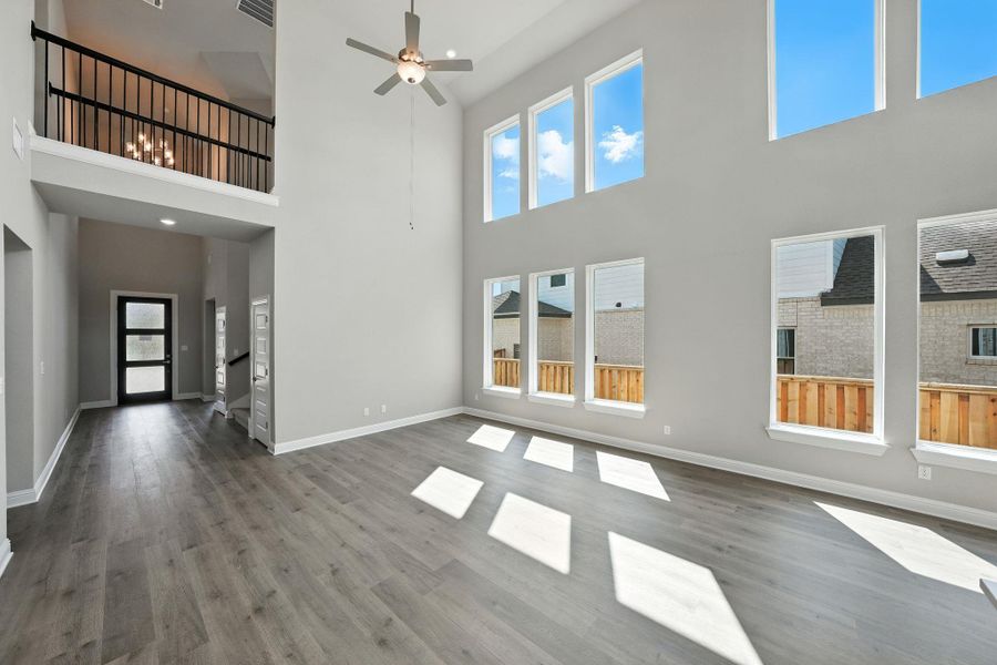 Unfurnished living room featuring wood finished floors, a high ceiling, and ceiling fan Unfurnished living room featuring wood finished floors, a high ceiling, and ceiling fan