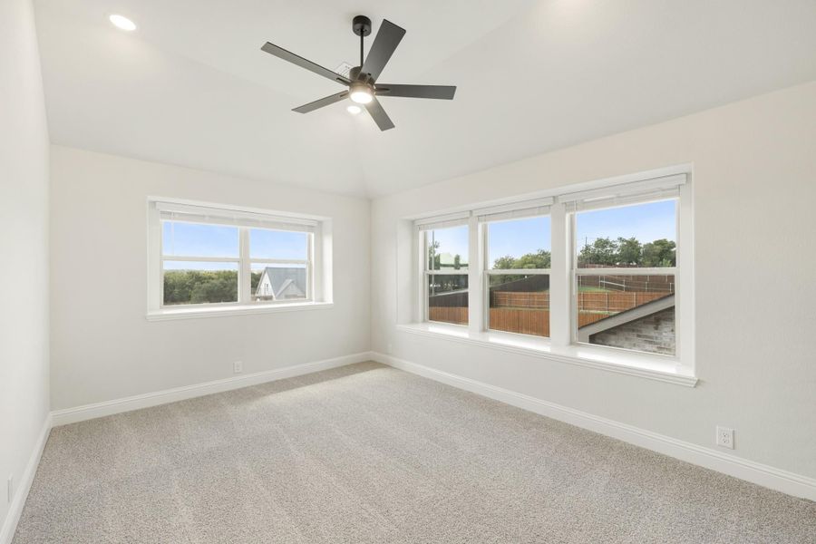Empty bedroom with carpet flooring, ceiling fan, and multiple windows with outdoor views