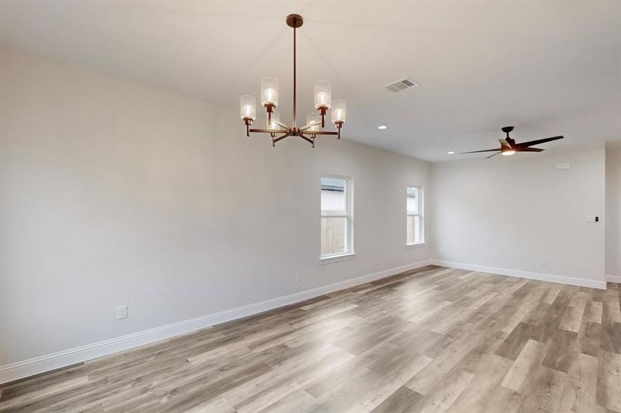 Empty room with ceiling fan with notable chandelier and light hardwood / wood-style floors