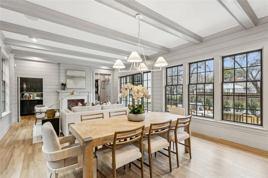 Dining room with light wood-style flooring, ornamental molding, beam ceiling, a notable chandelier, and a high end fireplace