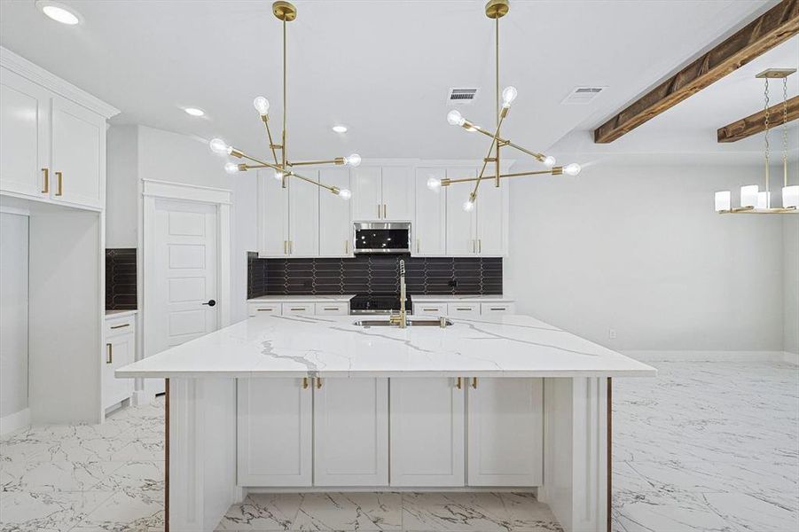 Kitchen featuring pendant lighting, light stone counters, an island with sink, and white cabinets