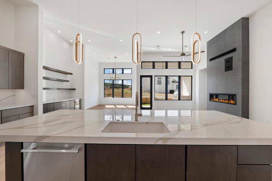 Kitchen featuring modern cabinets, dark wood finish cabinetry, dishwasher, a spacious island, and light stone countertops