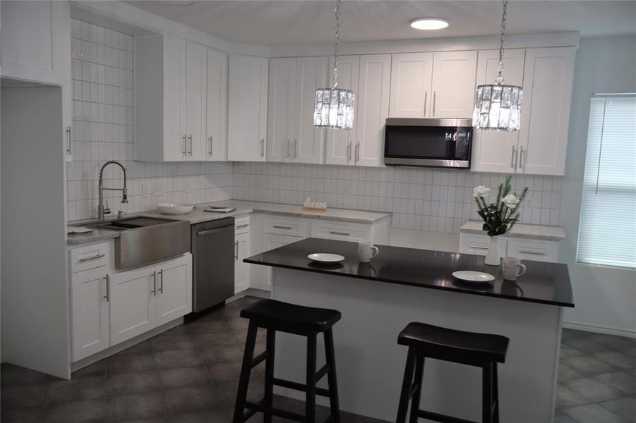 Modern kitchen featuring white shaker cabinetry, stainless steel appliances, a farmhouse sink, subway tile backsplash, and a dark countertop island