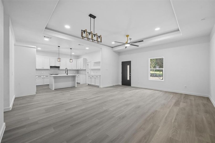 Unfurnished living room with a raised ceiling, light wood finished floors, a ceiling fan, and recessed lighting Unfurnished living room with a raised ceiling, light wood finished floors, a ceiling fan, and recessed lighting