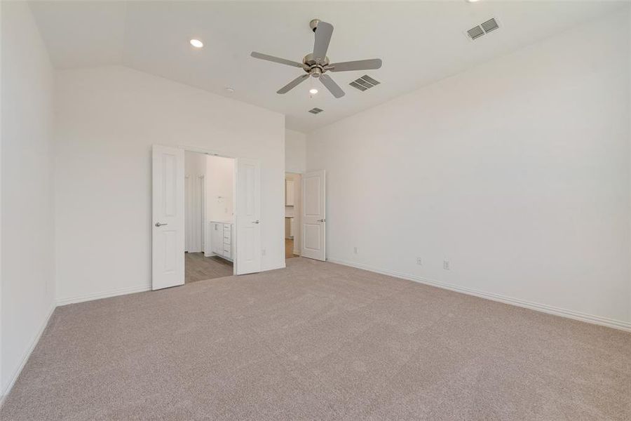 Unfurnished bedroom featuring lofted ceiling, ensuite bathroom, light colored carpet, and ceiling fan