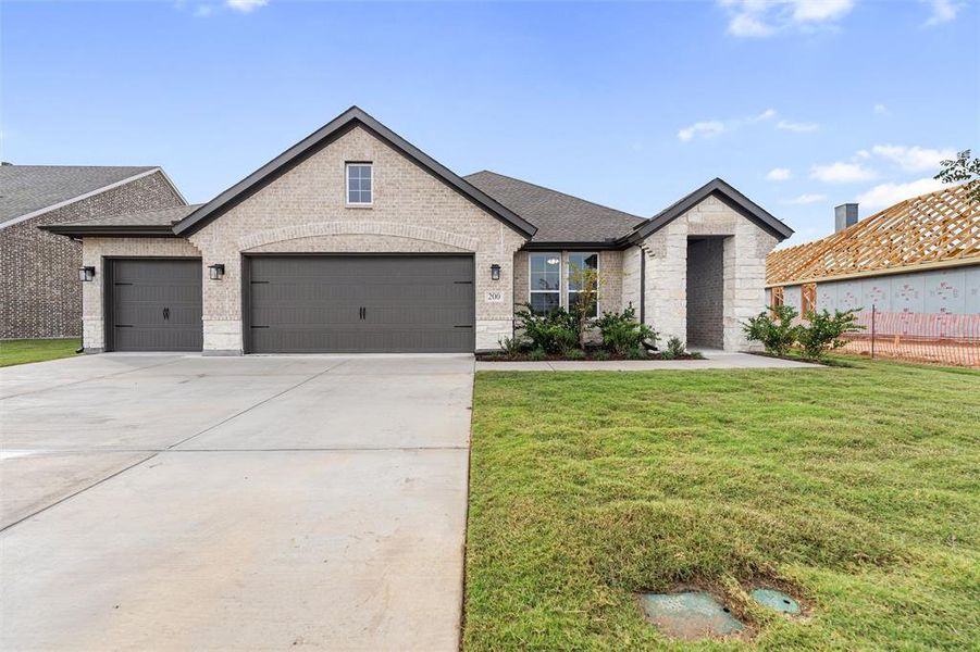 View of front of property with a front yard, concrete driveway, stone siding, brick siding, and a garage View of front of property with a front yard, concrete driveway, stone siding, brick siding, and a garage