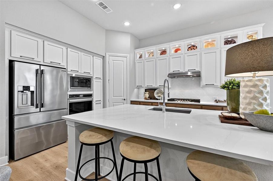 Kitchen with appliances with stainless steel finishes, under cabinet range hood, a kitchen breakfast bar, white cabinets, and recessed lighting Kitchen with appliances with stainless steel finishes, under cabinet range hood, a kitchen breakfast bar, white cabinets, and recessed lighting