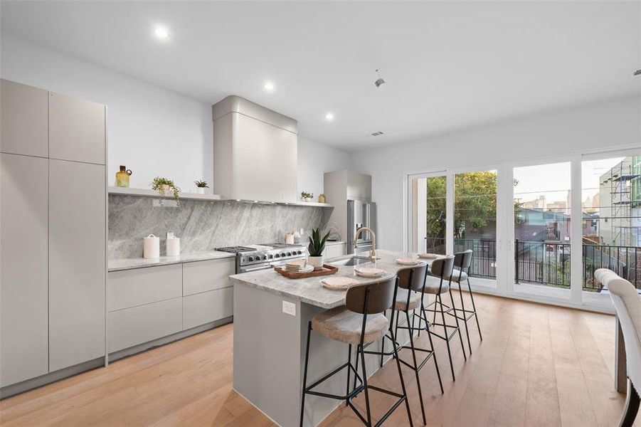 Kitchen with modern cabinets, backsplash, a breakfast bar, a kitchen island with sink, and light wood finished floors