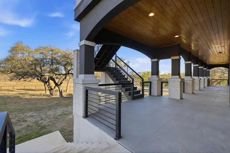 This property features an expansive covered patio with a wood plank ceiling and recessed lighting, supported by brick and dark-colored columns