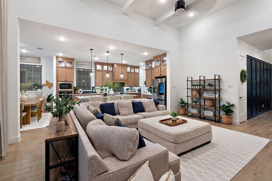The soaring family room features high ceilings with beams, an electric fireplace wall, and flows into a chef's kitchen with quartz countertops, oversized island, luxe pantry, Barley cabinetry with glass uppers, and GE Profile appliances including double ovens with built-in air fryer. The soaring family room features high ceilings with beams, an electric fireplace wall, and flows into a chef's kitchen with quartz countertops, oversized island, luxe pantry, Barley cabinetry with glass uppers, and GE Profile appliances including double ovens with built-in air fryer.