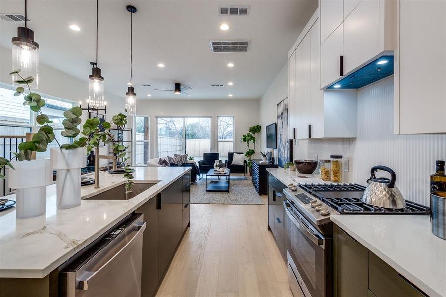 Kitchen with pendant lighting, white cabinets, light hardwood / wood-style floors, stainless steel appliances, and light stone countertops