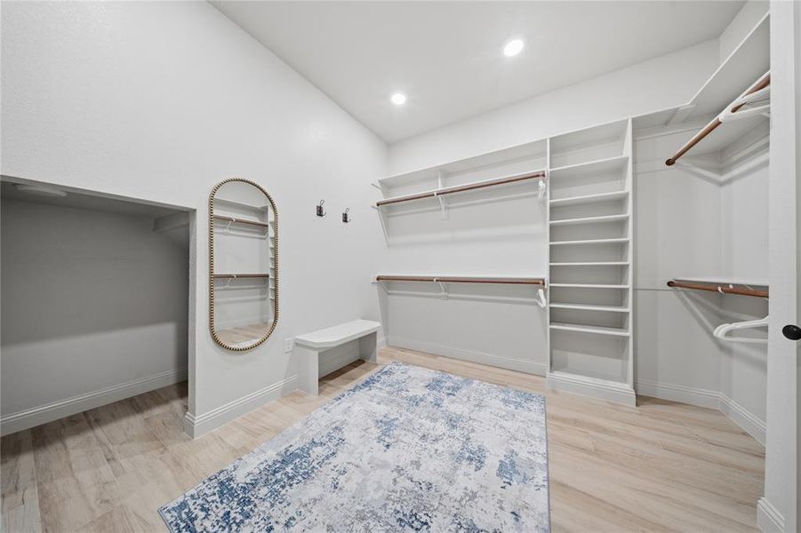 Spacious walk-in closet featuring light wood-finish flooring, recessed lighting, and extensive built-in shelving with hanging rods