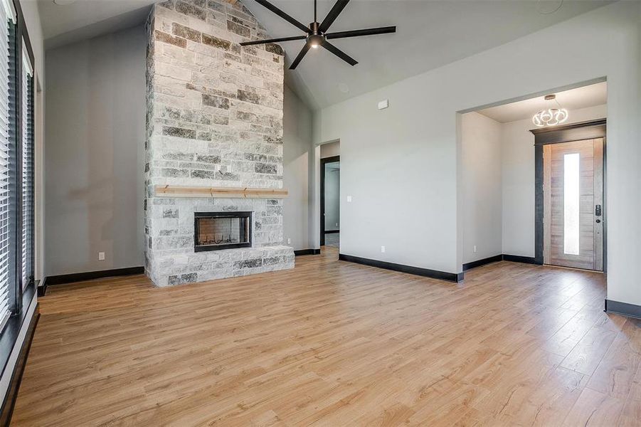 Unfurnished living room with a fireplace, ceiling fan with notable chandelier, high vaulted ceiling, and light hardwood / wood-style flooring