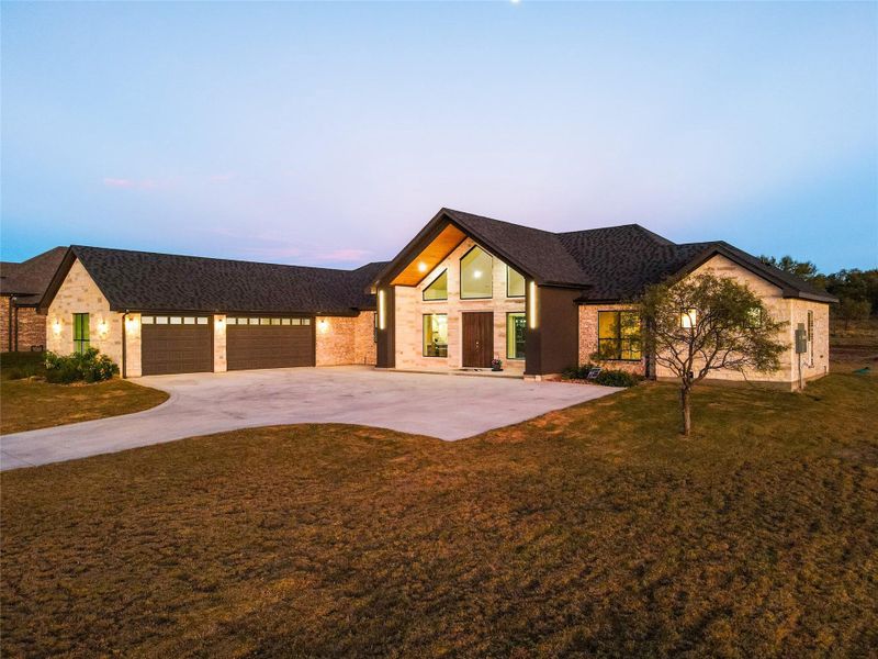 View of front of house with a front yard, driveway, a shingled roof, and stone siding