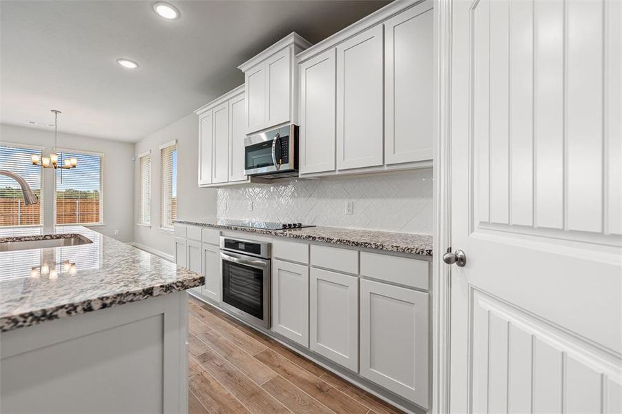Kitchen with pendant lighting, light stone counters, white cabinetry, backsplash, and appliances with stainless steel finishes Kitchen with pendant lighting, light stone counters, white cabinetry, backsplash, and appliances with stainless steel finishes