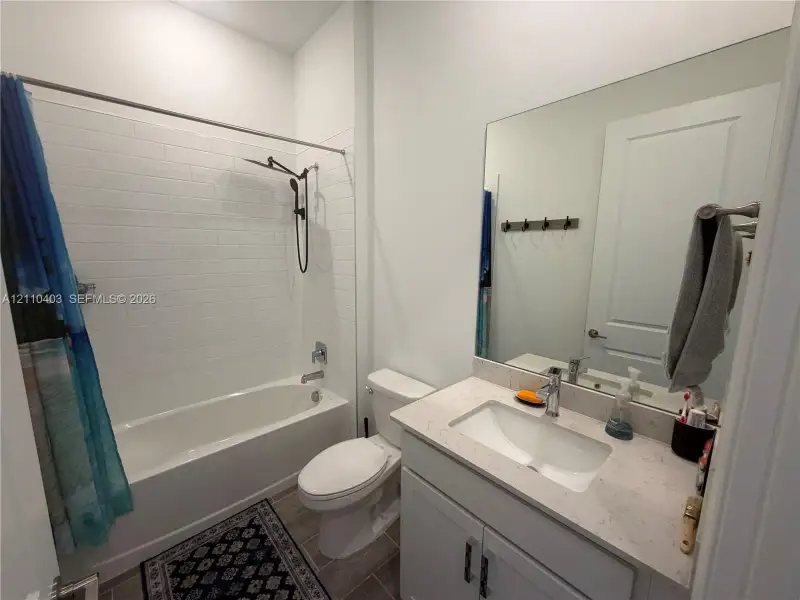 Bathroom featuring a vanity with a light-toned solid surface countertop and undermount sink, white cabinetry, subway tile bathtub surround, and wood-finish flooring