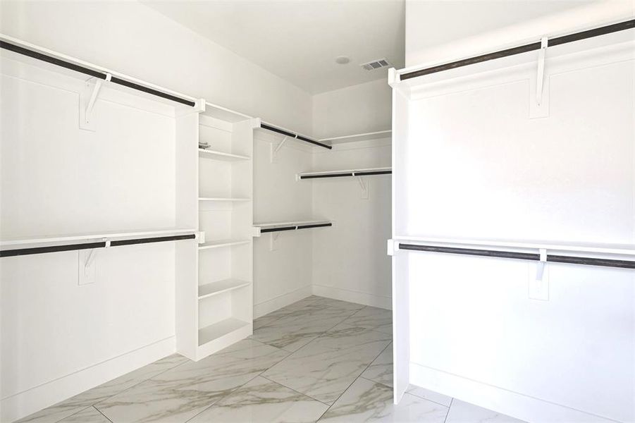 Spacious walk-in closet featuring white built-in shelving, multiple hanging rods, and patterned tile flooring