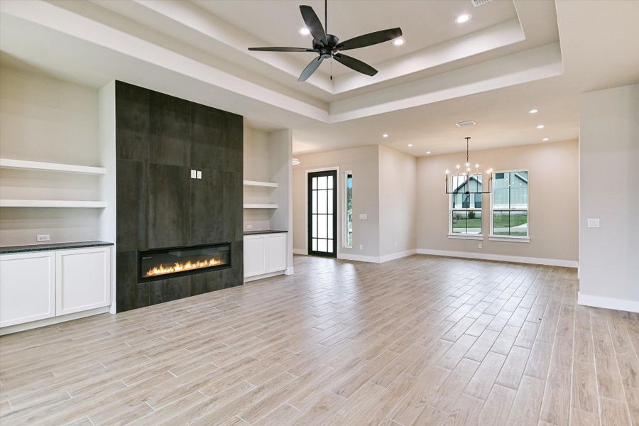 Unfurnished living room with wood finish floors, ceiling fan, a fireplace, hanging lights, and built in shelves