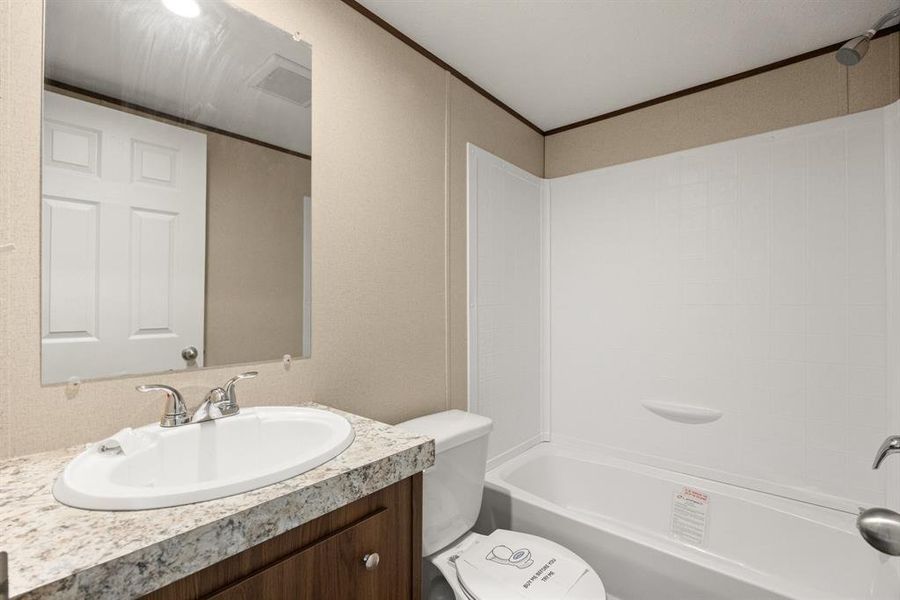 Bathroom featuring a white sink, chrome faucet, wood-finish vanity, light-toned countertop, and a white tub with shower surround