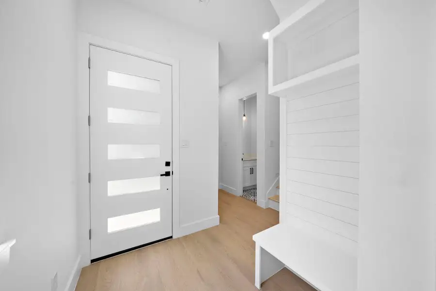 This entryway features a modern white door with frosted glass panels, light wood flooring, and built-in shelving for storage. A small hallway leads to additional rooms, offering a bright and welcoming space. This entryway features a modern white door with frosted glass panels, light wood flooring, and built-in shelving for storage. A small hallway leads to additional rooms, offering a bright and welcoming space.