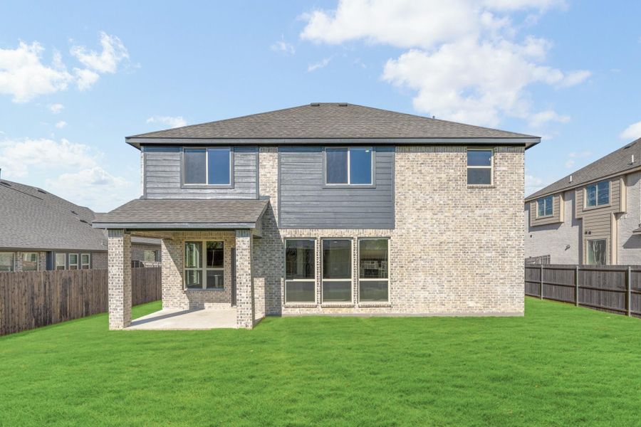 Two-story brick home rear view with covered patio, large windows, and fenced backyard with green lawn