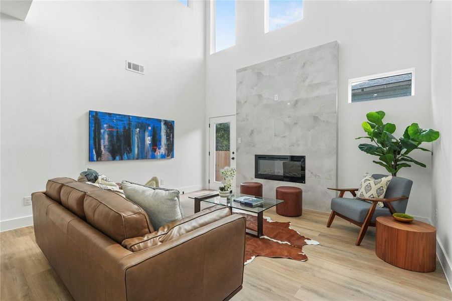 Living room featuring healthy amount of natural light, a high ceiling, light wood-type flooring, and a premium fireplace