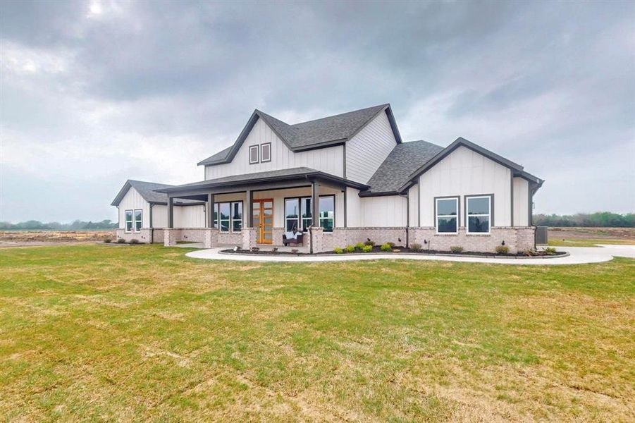 Modern inspired farmhouse featuring board and batten siding, covered porch, a front lawn, and roof with shingles Modern inspired farmhouse featuring board and batten siding, covered porch, a front lawn, and roof with shingles
