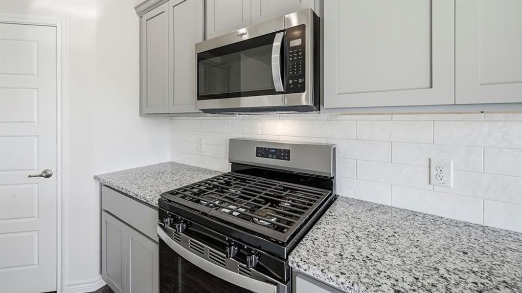 The kitchen features granite countertops, light gray cabinetry, stainless steel appliances, and a white subway tile backsplash