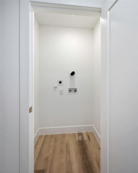 Clothes washing area with hookup for a washing machine, electric dryer hookup, and light wood-type flooring