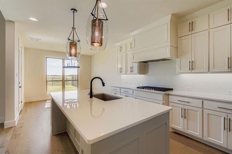 Kitchen featuring light wood-style floors, a center island with sink, light countertops, decorative light fixtures, and recessed lighting
