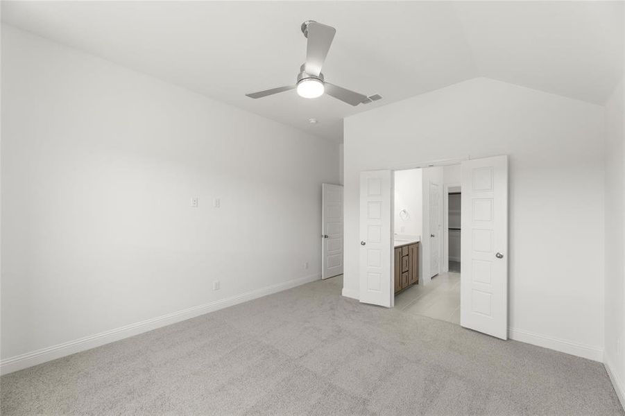 Unfurnished bedroom with connected bathroom, ceiling fan, vaulted ceiling, and light colored carpet