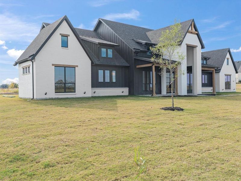 Back of property featuring a lawn, board and batten siding, brick siding, and a shingled roof