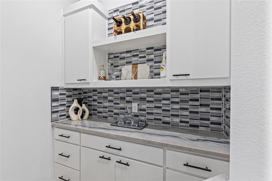 Detailed view of tasteful backsplash, white cabinets, a textured wall, light stone countertops, and open shelves