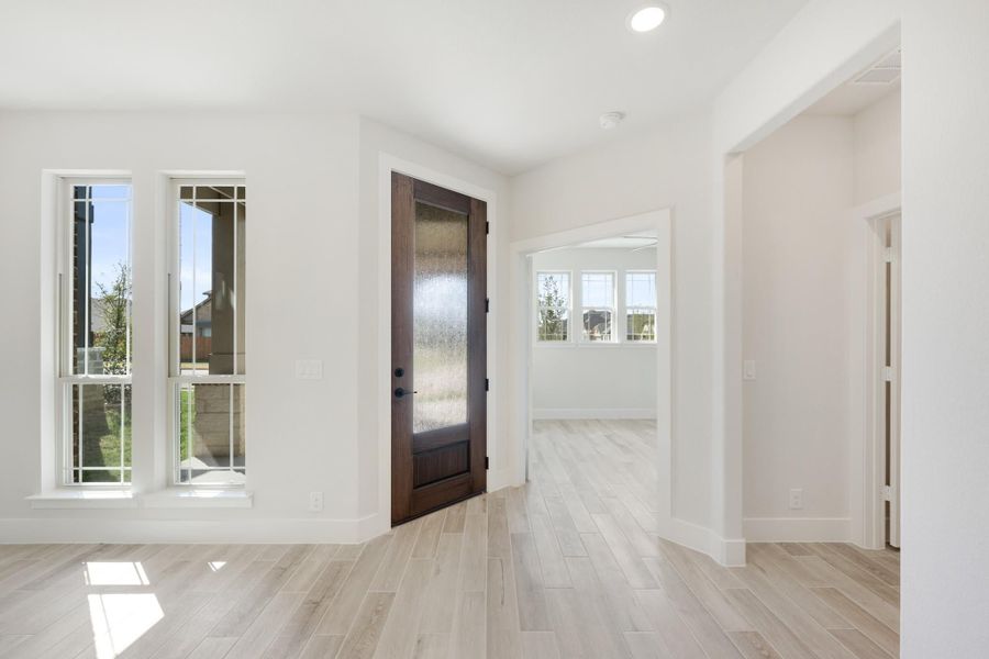 Bright entryway with dark wood front door, frosted glass panel, white walls, and light wood-look tile floors