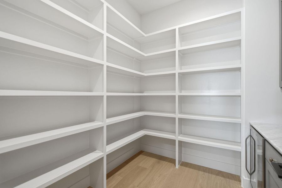 Custom built-in shelving wraps around this walk-in pantry featuring light hardwood flooring.