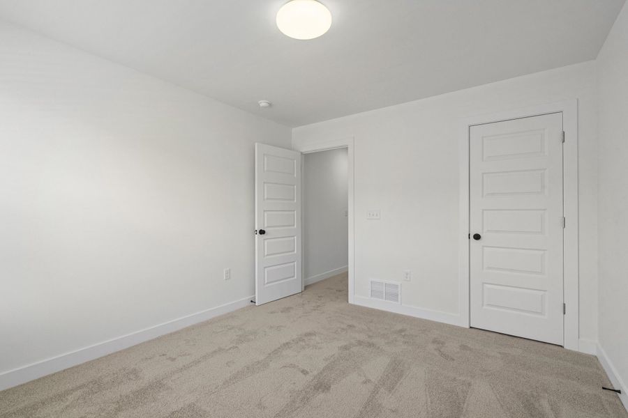 Neutral tone interior featuring plush carpet flooring, white walls, and bright overhead lighting