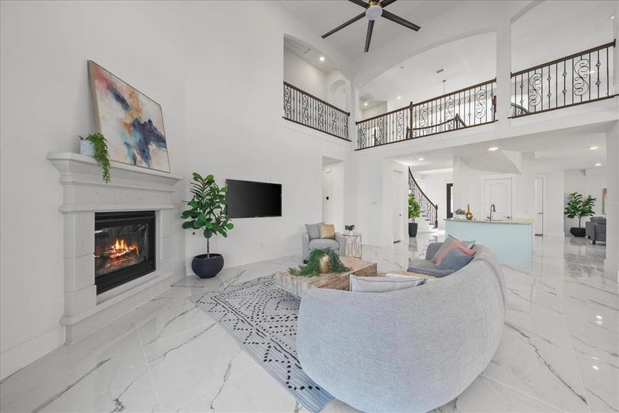 Living room featuring a gas fireplace, a towering ceiling, stairway, light marble finish flooring, and recessed lighting Living room featuring a gas fireplace, a towering ceiling, stairway, light marble finish flooring, and recessed lighting